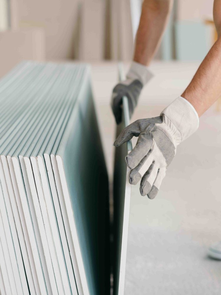 Builder taking a sheet of chip board from a stack in a close up view of his gloved hands in a new build house